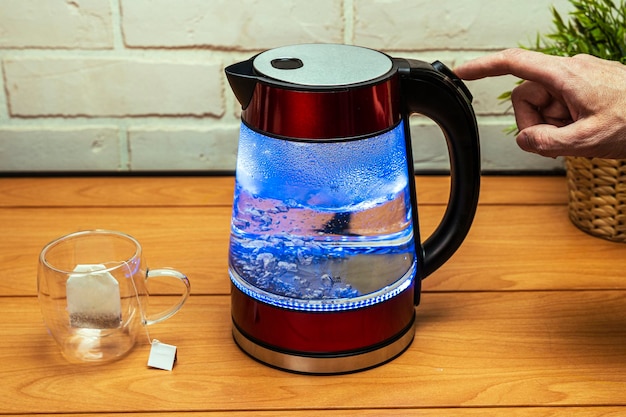 Man turns off the heating button of a modern glass electric kettle