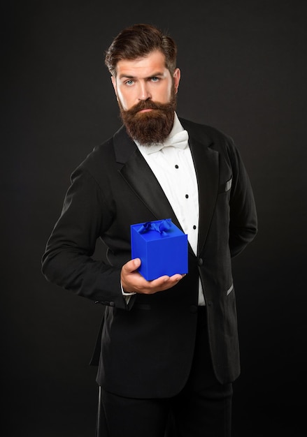 Man in tuxedo bow tie formalwear on black background with box.\
valentines day.