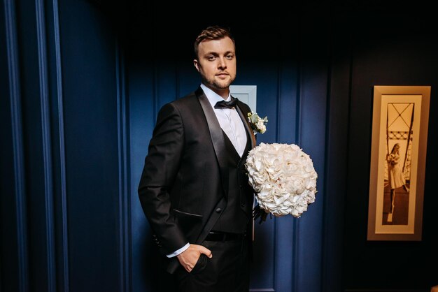 Photo a man in a tuxedo holds a white flower bouquet