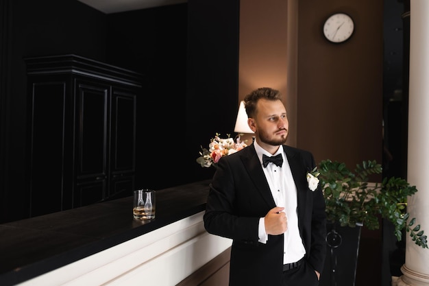 A man in a tuxedo stands in front of a clock that says'the groom '