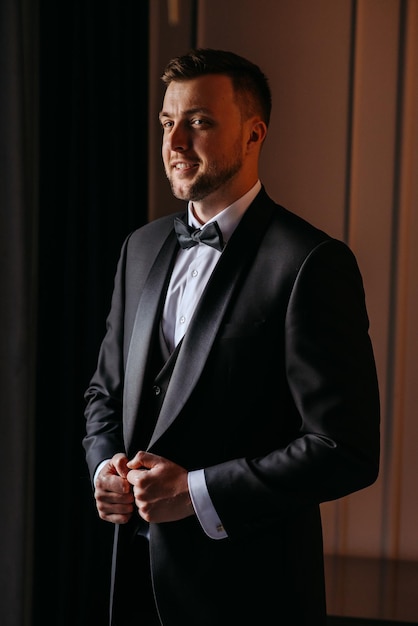 Photo a man in a tuxedo stands in front of a window