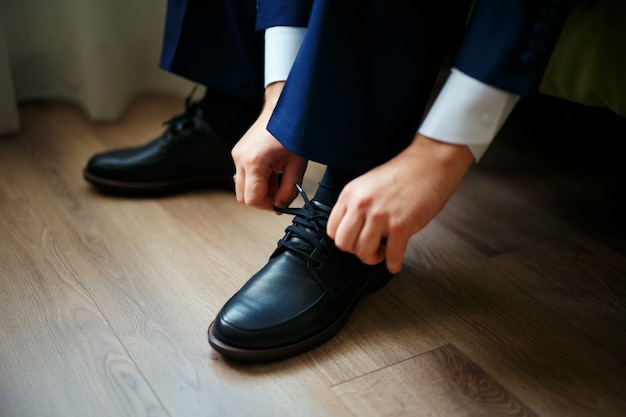 木の床の黒い靴にひもを結ぶ男