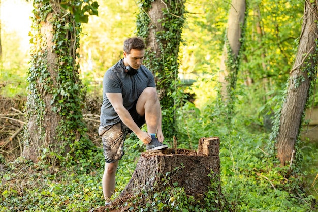 Foto uomo che lega i lacci delle scarpe sul tronco di un albero nella foresta