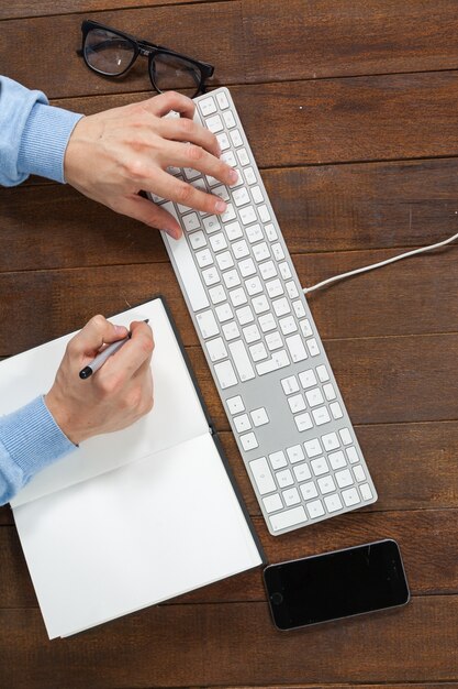 Man typing on keyboard and writing in diary