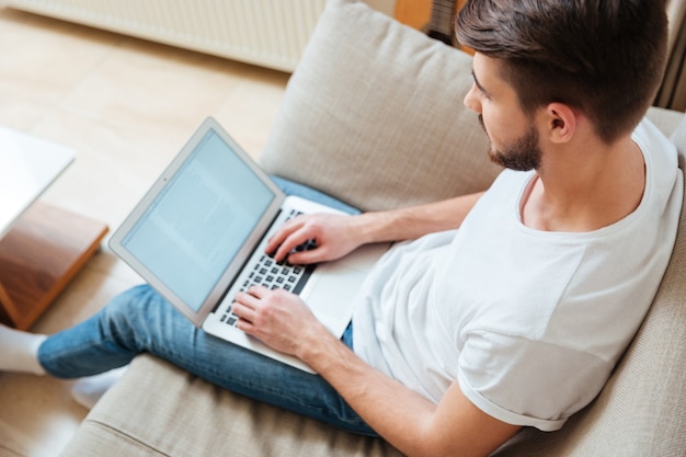 Man typing text on laptop computer on the sofa at home