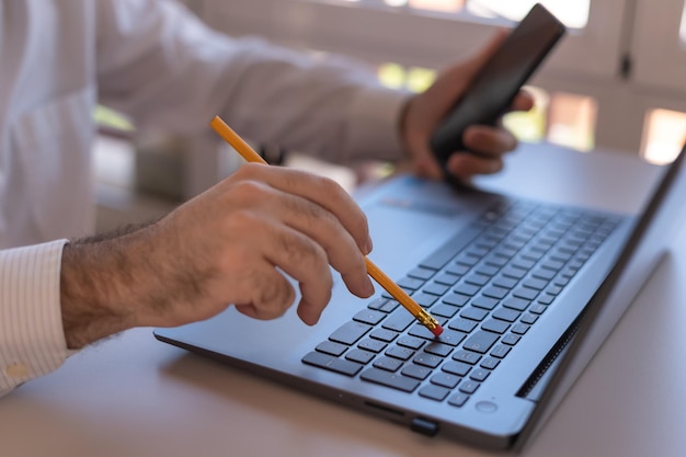 Man typt op een laptop met zijn pen en controleert de mobiele telefoon tijdens telewerken