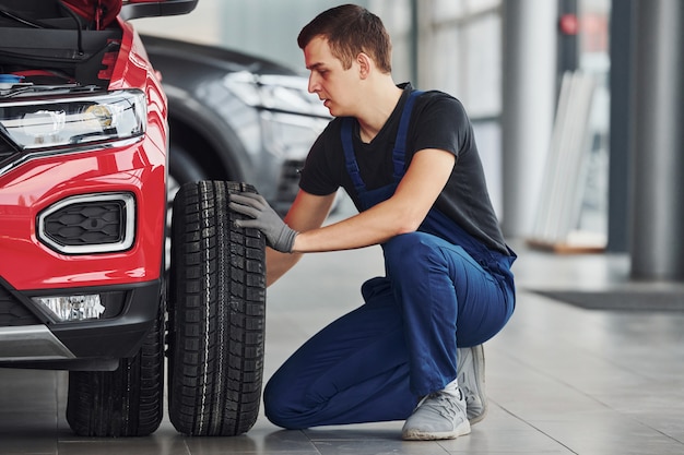 Man in uniform changing tire of automobile. Conception of car service