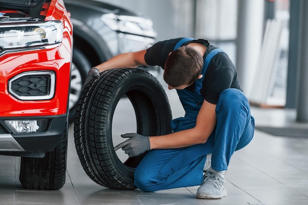 Man in uniform changing tire of automobile Conception of car service