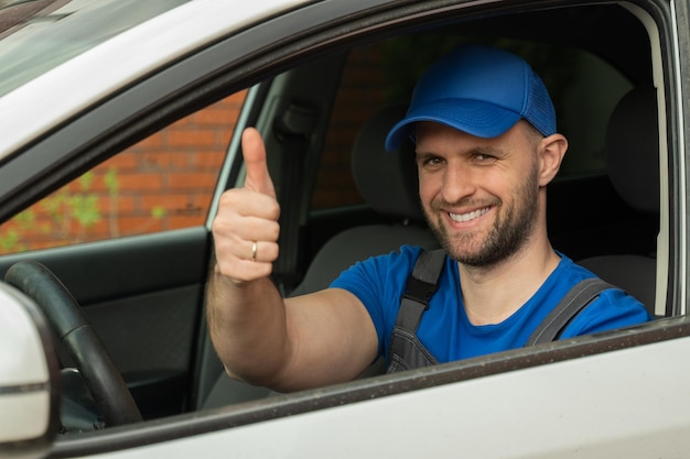 man in uniform sits on driver seat looking at camera and showing thumbup closeup repairman smiles