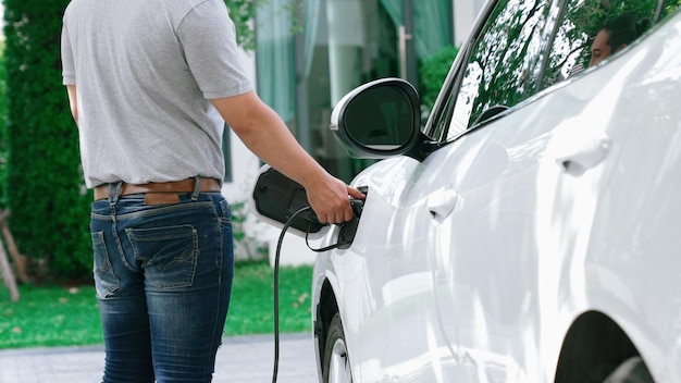 A man unplugs the electric vehicle's charger at his residence Concept of the use of electric vehicles in a progressive lifestyle contributes to a clean and healthy environment