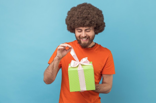 Man unwrapping birthday present for celebrating holiday pulling ribbon looking at gift