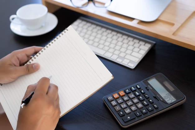 Man use calculator  make note with calculate about cost  in office Close up