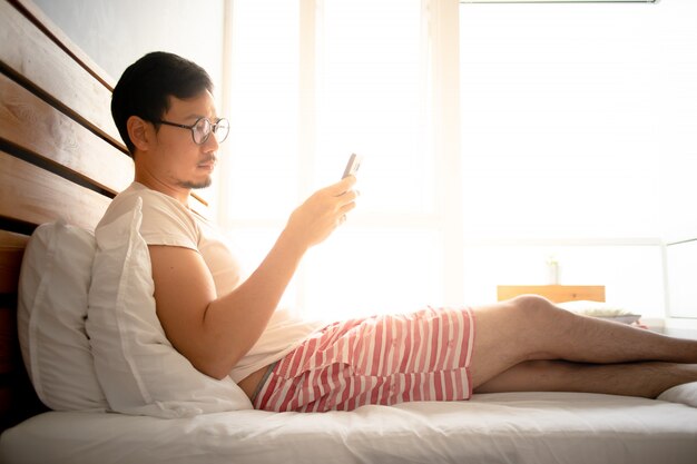 Man use his smartphone and relax on his bed.