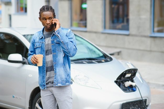 Man use smart phone while waiting and power supply connect to\
electric vehicles for charging the battery in car