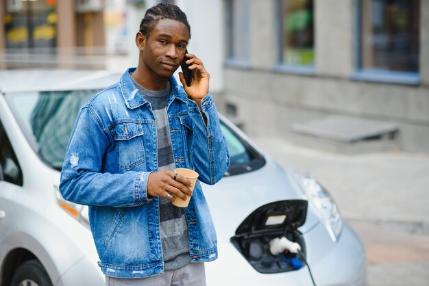 man use smart phone while waiting and power supply connect to electric vehicles for charging the battery in car