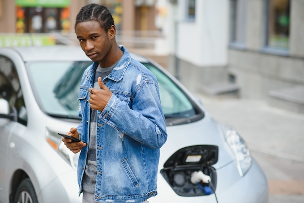 남자는 기다리는 동안 스마트 폰을 사용하고 전원 공급 장치는 자동차의 배터리를 충전하기 위해 전기 자동차에 연결합니다.
