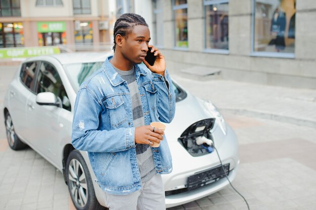 Man use smart phone while waiting and power supply connect to
electric vehicles for charging the battery in car