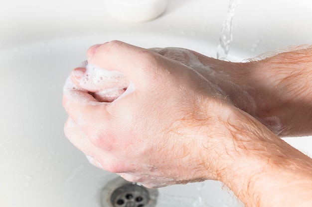 Man use soap and washing hands under the water tap. Hygiene concept hand detail.