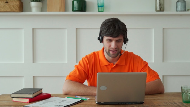 Man uses a headset to talk online at his workplace, confident man sits at the office desk and looks at laptop screen