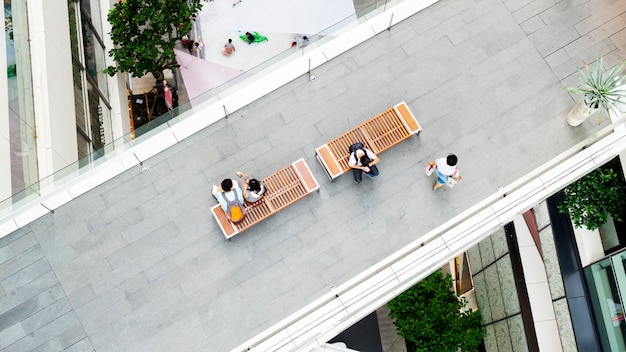 Man uses smartphone and couple of teen sit on bench at pedestrian walkway on top aerial view