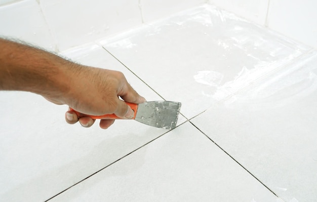 Photo man uses trowel to remove old grout. replace the old grout between the tiles. mining tiles for rerou