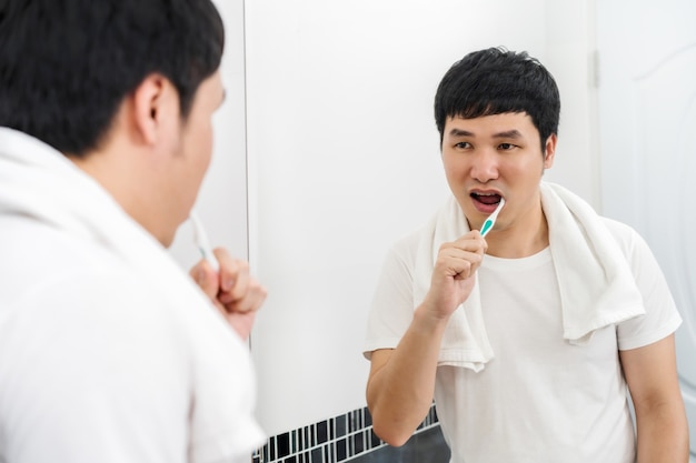 Uomo che usa lo spazzolino da denti per lavarsi i denti nello specchio del bagno