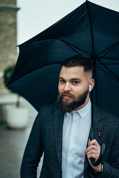 Foto uomo che usa un airpod mentre tiene un ombrello nero