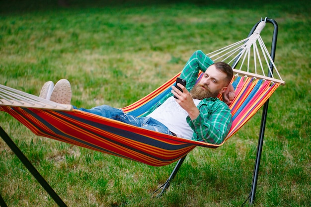 Man using an app on his mobile phone white swinging in a hammock