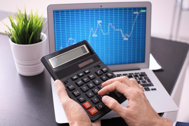 Man using calculator near laptop with stock chart data on screen Forex concept