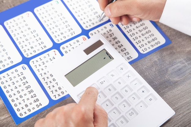 Man using calculator with a multiplication table.