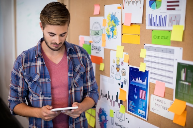 Man using digital tablet next to the board with sticky notes in office