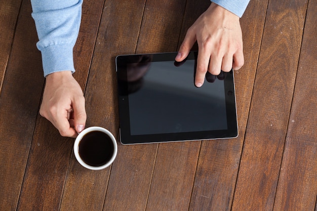 Man using digital tablet while having cup of coffee