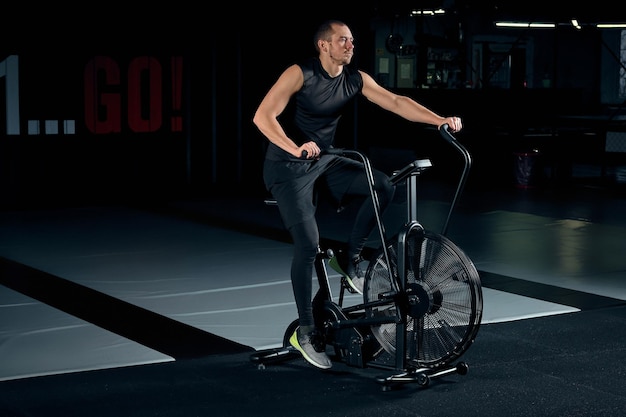 Man using exercise bike at the gym. Fitness male using air bike for cardio workout at Functional training gym.