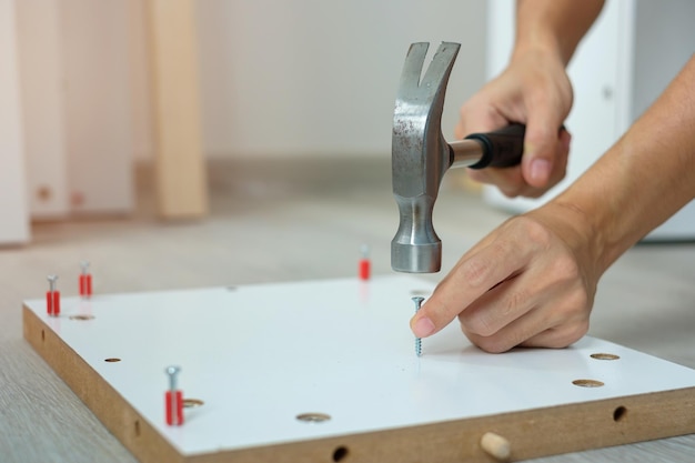 Man using hammer hammering a nail into wooden boards assembling or repairing furniture at home DIY Renovation repairing and development home or apartment concepts