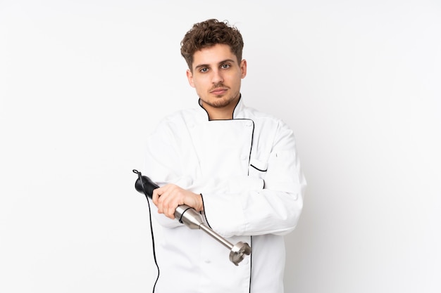 Man using hand blender isolated on white wall keeping arms crossed