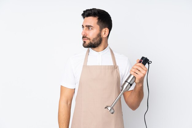 Man using hand blender isolated on white wall looking side