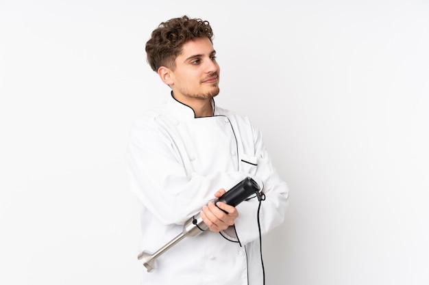 Man using hand blender isolated on white wall looking to the side