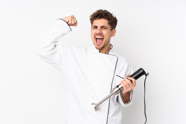 Man using hand blender on white wall celebrating a victory