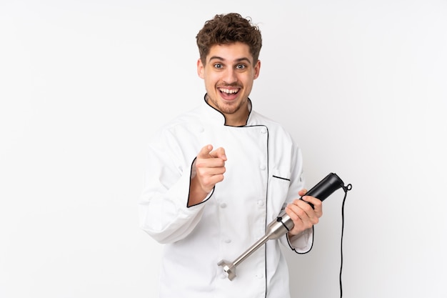 Man using hand blender on white wall points finger at you