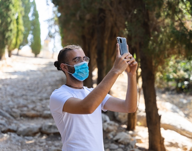 携帯電話を使ってマスクと白いTシャツを着て写真を撮る男性
