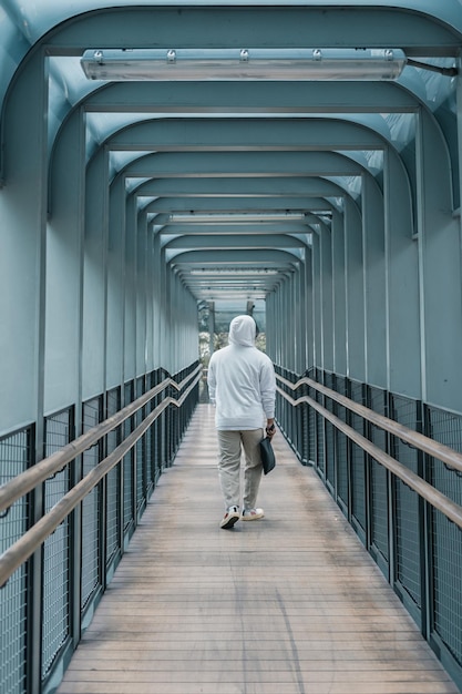 man using hoodie walking on pedestrian bridge