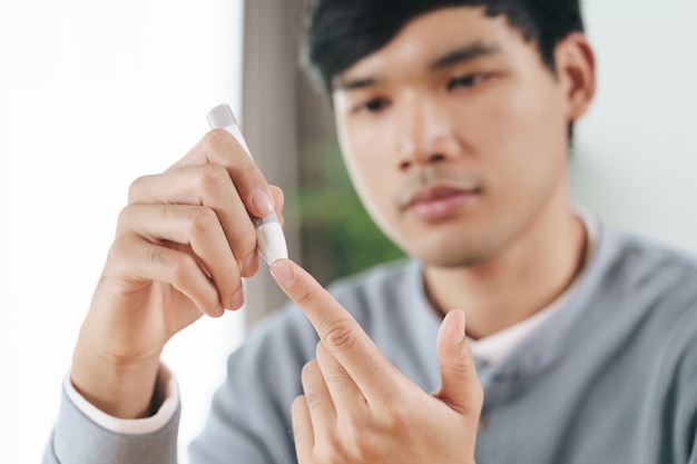 血糖値計、糖尿病の概念によって血糖値をチェックするために指にランセットを使用している男性