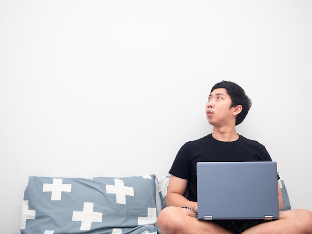 Человек, использующий ноутбук на кровати, чувствует себя взволнованным, глядя на копировальное пространство на белом фоне
