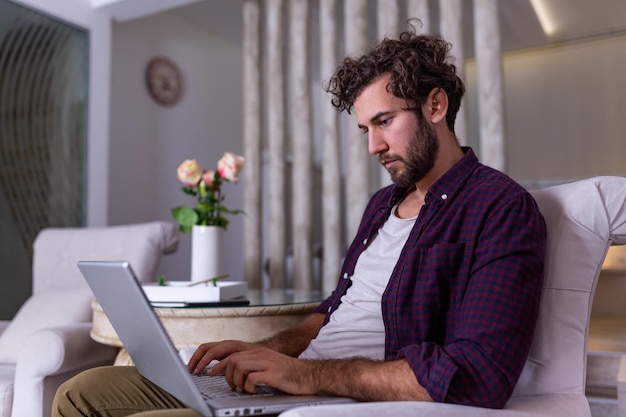 Man using laptop computer, working at home. Worried about finances. Handsome man with beard working at home on project, he is sitting on sofa looking at his laptop in front of him. Focus on the man