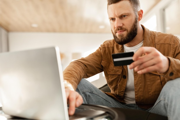 Man using laptop and credit card shopping online sitting indoors