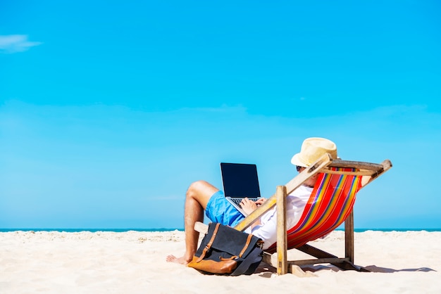 A man using laptop on the tropical beach on vacation. 