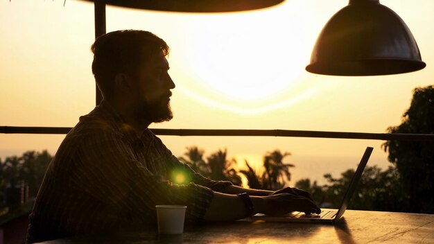 Photo man using laptop while sitting at restaurant against sky during sunset