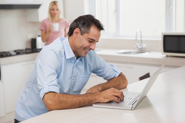 Man using laptop while woman drinking coffee in kitchen