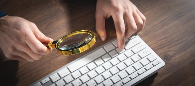 Man using magnifying glass and typing in computer keyboard Concept of searching internet