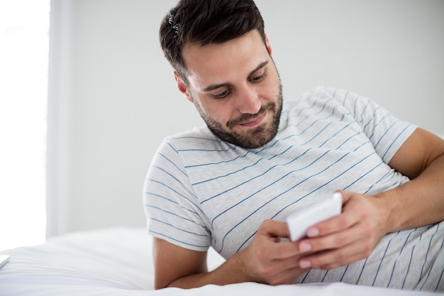 Man using mobile phone on bed in bedroom